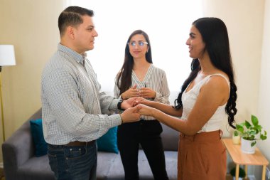 Arka planda psikologlarıyla çift terapisi sırasında el ele tutuşan ve barış yapan genç Latin çift.