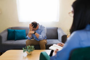 Depresyonda olan bir adam terapi seansında psikolog notlar alırken psikolojik destek alıyor.