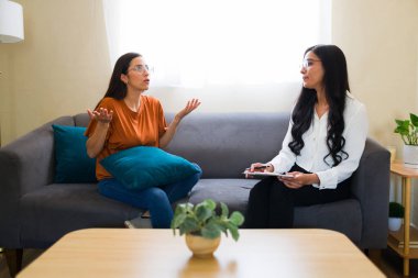 Psikoterapi seansı sırasında rahat bir koltukta otururken zihinsel sağlık sorunlarını açıklayan genç bir kadın.