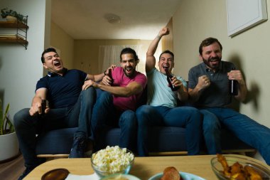 Yoğun erkek arkadaşlar sıcak bir oturma odasında birlikte yoğun bir spor maçı izlerken soğuk bira içip tezahürat yapıyorlar.