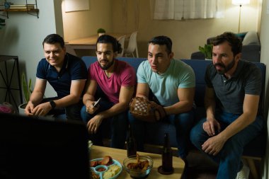 İspanyol erkek arkadaşlar televizyonda beyzbol maçı izliyor, sıcak bir ev ortamında atıştırmalık ve içeceklerin keyfini çıkarıyorlar.