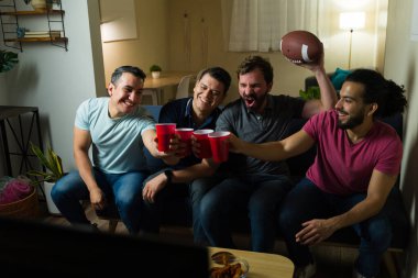 Heyecanlı erkek arkadaşlar kanepede oturup, TV 'de maç izleyip, topla tezahürat yapıyorlar, içkilerle kadeh kaldırıyorlar ve evlerinde eğleniyorlar.