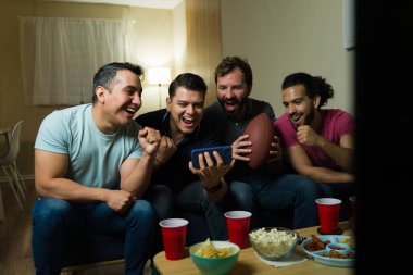 Dört İspanyol 'un tezahürat yaptığı ve cep telefonuyla maç skorunu izlerken evde atıştırmalık ve içki içtiği bir grup.