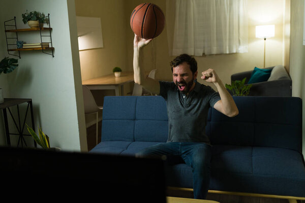 Мужчина веселится и играет в баскетбол во время просмотра спортивной игры по телевизору в гостиной