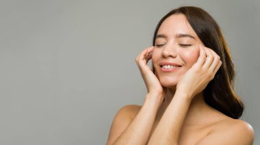 Güzel bir genç kadının portresi nazikçe yüzüne dokunuyor elleri, gözleri kapalı, cilt bakımının keyfini çıkarıyor.