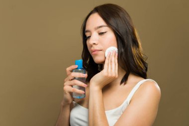 Genç bir kadın günlük cilt bakımı için pamuk pedi ve toner kullanıyor. Sağlıklı bir cilt ve doğal bir parlaklık sağlıyor.