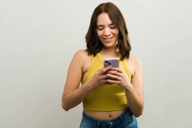 Stüdyoda, elinde akıllı telefon tutan ve kullanan gülümseyen genç bir kadının cep telefonu teknolojisinden ve internet bağlantısından hoşlandığı bir fotoğraf.