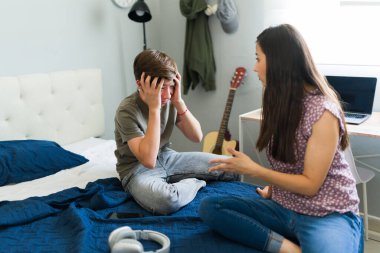 Üzgün genç çocuk evde annesiyle konuşurken elleriyle kulaklarını tıkıyor.
