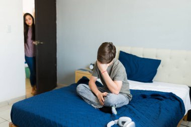 Annesi onu kapı eşiğinden izlerken, şaşkına dönmüş genç bir çocuk elleriyle yüzünü kapatıyor.