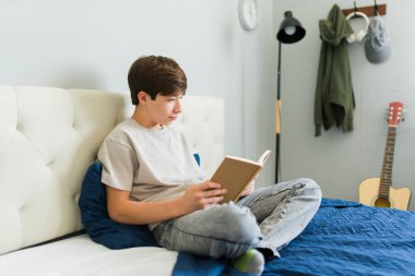 Genç, sıcak ve davetkar bir yatak odasında rahat bir yatakta uzanıp huzurlu bir anın tadını çıkarırken büyüleyici bir kitaba dalmış.