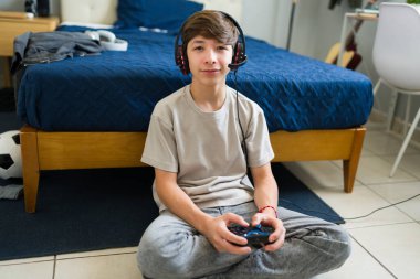 Kulaklık takan ve yatak odasında video oyunu oynarken kumanda kullanan bir genç. Evde eğleniyor.