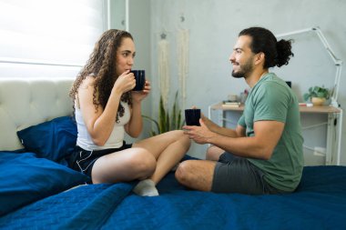 Genç İspanyol çift yatakta rahatlıyor ve kahve içiyor. Sabahları birlikte sakin bir anın tadını çıkarıyorlar.