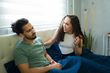 Yatakta birlikte otururken erkek arkadaşıyla tartışan, ilişki sorunları yaşayan ve iletişim sorunları yaşayan bir kadın.