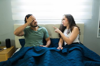 Kızgın Latin kadın erkek arkadaşını azarlıyor ve yatakta ilişki problemlerini tartışırken onu işaret ediyor.