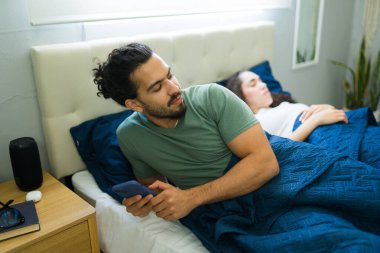Genç adam akıllı telefon kullanıyor ve partnerinden bir şeyler saklıyor. Evde yanında uyuyor.