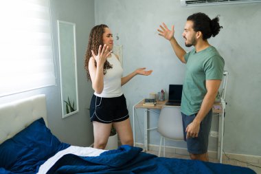 Genç İspanyol çift rahatsız edici ifadelerle tartışıyor, yatak odalarında elleriyle el kol hareketi yapıyorlar.