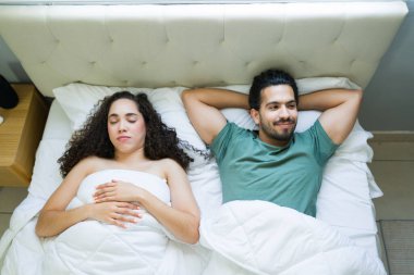 Genç bir İspanyol çiftin yatakta yatarken, erkek uyanıkken ve hayal kurarken kadının huzur içinde uyuduğu yüksek açılı görüntüsü.