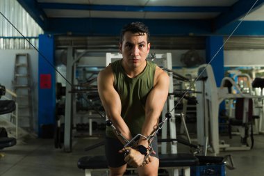 Genç adam kablolu yayın makinesinde göğüs kaslarını çalıştırıyor. Spor salonunda yoğun bir odak ile çalışıyor.