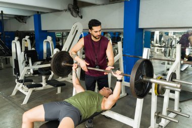 Spor salonunda göğüs presi egzersizi yapan bir adama kişisel antrenör asistanı. Fitness, güç antrenmanı ve egzersiz rutinine odaklan.