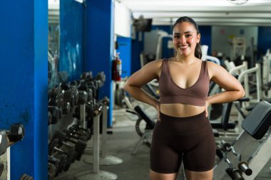 Genç bir kadın, sağlık kulübündeki yoğun güç eğitiminden sonra kendinden emin bir şekilde gülümsüyor, sağlık, sağlık ve motivasyon saçıyor.