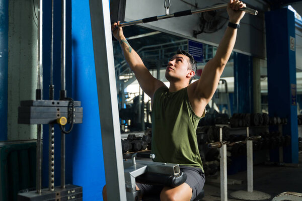 Male athlete building upper body strength, doing lat pulldown exercise on weight machine for fitness workout