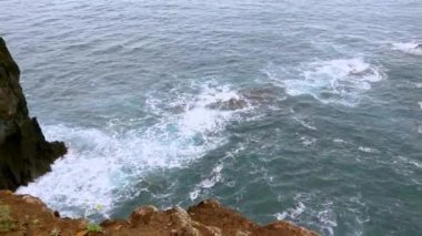 Doğanın güzel sahil şeridi manzarası. Kayalar ve adanın bir kısmı okyanus tarafından yıkanır. Madeira, Portekiz. Doğa geçmişi. Okyanus dalgaları kırılır ve büyük taşlarla köpük oluşturur. Okyanus suyu