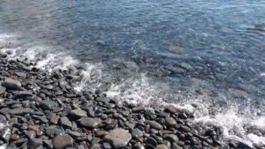 Okyanus ya da deniz kıyısındaki taştan bir plaja yakın çekim. Denizde dinlen. Kayalık sahilin güzel bir manzarası, su kıyıya vuruyor.