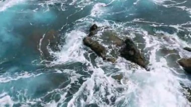 Aerial view footage over the turquoise waves of the ocean or sea. Waves crash over the rocks and the beach. Storm. Power of nature