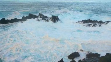 Taşlardaki dalgaları yavaş çekimde kırıyor. Beyaz köpük. Su ve dalga damlaları