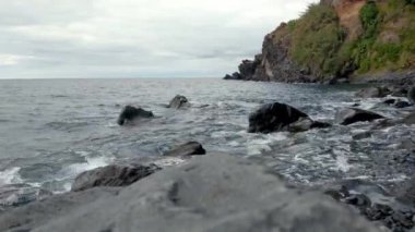 Adadaki volkanik kayaların Rocky sahili. Dalgalar kayaların üzerinde süzülür