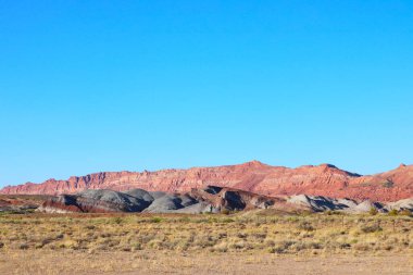 Arkaplanda açık mavi bir gökyüzüne karşı genişleyen bir sıradağları yakalayan bir fotoğraf. Dağların engebeli zirveleri, sakin gökyüzüne karşı çarpıcı bir kontrastlık yaratır..