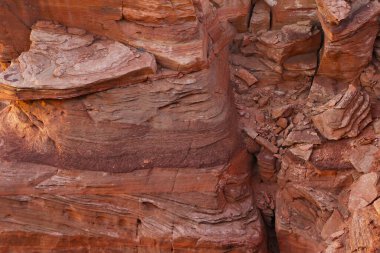 Temiz bir gökyüzünün altında çorak bir çöl arazisinin ortasında duran büyük bir kaya oluşumunu tasvir eden bir fotoğraf. Kaya oluşumu kayalık ve engebeli, etrafındaki düz kumlu araziyle çelişiyor..