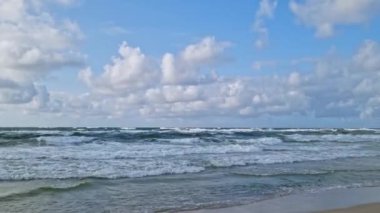 Dalgalı dalgaların dalgalı bulutlarla dolu bir gökyüzünün altında kıyıya çarpmasıyla sakin bir sahil manzarası, akşam karanlığında kıyı manzaralarının dinamik ama dinamik doğasını vurguluyor..