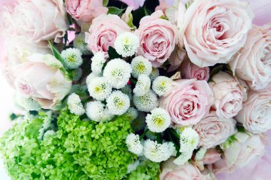 Bir buket pembe ve beyaz çiçek ahşap bir masada zarif bir şekilde sergilenir. Çiçekler taze, narin yaprakları ve yeşil yaprakları var. Çok güzel bir süs yapıyorlar..