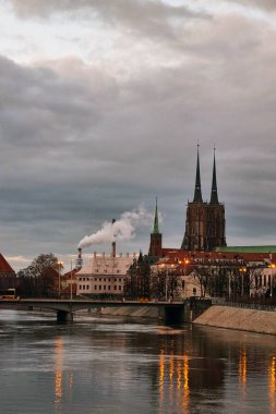 Wroclaw, Polonya, 15 Şubat 2024: Yükselen gökdelenler ve yüksek binalarla çevrili hareketli bir şehir içinden bir nehir akar. Su, şehir manzarasını keserek doğa ile insan yapımı yapılar arasındaki zıtlığı gözler önüne seriyor..