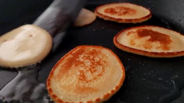 Close-up shot of several pancakes being cooked on a hot griddle. the golden-brown surface of the pancakes contrasts with the dark cooking surface. ideal for use in culinary blogs, recipe cards, and