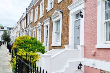 Londra, Birleşik Krallık, 24 Mart 2024: Zarif mimari detayların yer aldığı bir dizi büyüleyici renkli konak evinin canlı sokak manzarası. Sahne pastel renkli cepheler, beyaz süsler ve bereketli yeşillik içeriyor, kentsel canlanmanın özünü yansıtıyor.