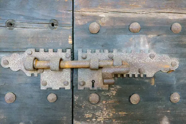 Kaliteli demir kilit ve cıvata mekanizması olan eski ahşap bir kapı. Bu yakın plan vurgular karmaşık metal işleri ve eski dokular, mimari çalışmalar, tarihsel referanslar veya tasarım ilhamı için ideal.