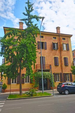 Modena, İtalya, 12 Mayıs 2024: Büyük pencereli ve panjurlu geleneksel mimari sergilenen antika İtalyan konut binası. Bereketli bir ağaç şehir sahnesine yeşillik katarken, park halindeki arabalar bir kısmının altında huzurlu bir mahalle kurulduğunu öne sürüyor.