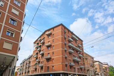 Bologna, İtalya, 16 Mayıs 2024: Belirgin kırmızı tuğla cephe, birden fazla balkon ve açısal tasarım içeren şehir konutları. Düşük bir açıyla temiz bir gökyüzüne, mimari detaylara ve şehir altyapı elemanlarına karşı yakalanmış, mükemmel.