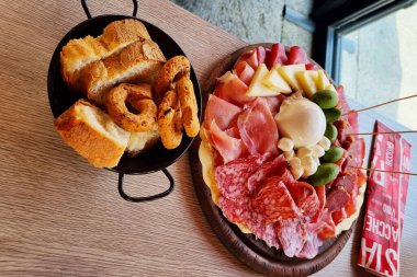 Modena, İtalya, 12 Mayıs 2024: Çeşitli pişirilmiş et, peynir ve aromalı ekmeklerin yer aldığı gurme antipasto tabağı. Yemek sunumları, restoran menüleri ve yemek kitapları için mükemmel. Prosciutto, salam, zeytin, mozzarella peyniri
