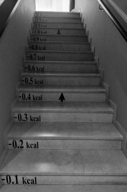 Bolonya, İtalya, 18 Mayıs 2024: Her basamakta kalori sayımı etiketli siyah beyaz mermer merdiven kalori yanığı ile spor ve egzersiz. Her adım yukarı doğru ilerledikçe yakılan kalorilerle işaretlenir.