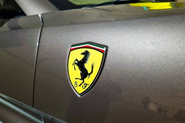 Modena, İtalya, 12 Mayıs 2024: Metalik kahverengi bir spor arabanın yanında ferrari amblemi sergilenmektedir. lüks aracın markasını ve şık tasarımını sergiliyor. Yüksek performans ve prestijle eş anlamlı sembolik at logosunu vurguluyor..