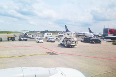 Bologna, İtalya, 18 Mayıs 2024: Ryanair uçaklarına hizmet veren yer destek ekipmanları ve araçları gösteren yoğun bir havaalanı önlüğü. Yolcu bindirme köprüleri ve destek kamyonları, kısmen CI 'nin altında uçağa binmeye hazırlanan uçakların net bir görüntüsüyle görülebilir.