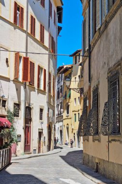 Florence, Italia, 11 Mayıs 2024: Açık mavi gökyüzü altında renkli panjurları olan eski Avrupa caddeleri manzarası. Parke taşı yolu, manzaralı mimari boyunca esiyor. Yolculuk için mükemmel sakin bir atmosfer sunuyor. 