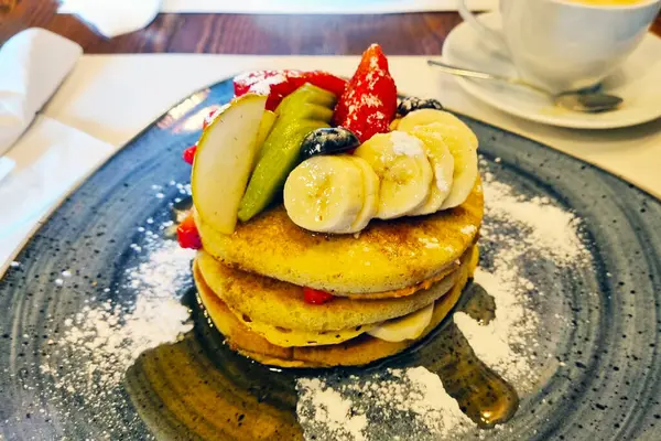 Taze muz dilimleri, elma parçaları, çilek ve yabanmersinli lezzetli bir yığın krep. Benekli seramik bir tabakta servis edilir ve hafif pudra şekeriyle toz alınır. Kahvaltı menüleri ve mutfak promosyonları için ideal.