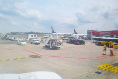 Bologna, İtalya, 11 Mayıs 2024: Ryanair uçağını çevreleyen yer servis araçlarıyla dolu havaalanı pisti. Bulutlu bir gökyüzünün altında çalışan bagaj arabaları, bir mekik ve personel, seyahat ve ulaşım sektörünü temsil ediyor.