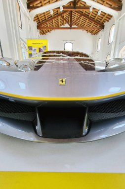 Modena, İtalya, 14 Mayıs 2024: Ferrari spor arabası bir otomotiv galerisinde sergilendi parlak ön ızgarası ve sembolik amblemi. Modern iç ve ahşap tavan, aracın birinci sınıf tasarımı ve zanaatkarlığını vurgulayarak çarpıcı bir kontrast oluşturuyor.