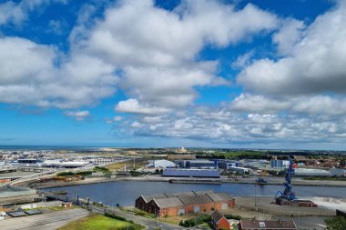 Calais, Fransa, 22 Haziran 2024: Kısmen bulutlu mavi gökyüzü altında depo, vinç ve sanayi binalarının yer aldığı nehir boyunca uzanan kıyı sanayi bölgesinin manzarası. Sahne sergileniyor.