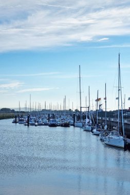 Calais, Fransa, 22 Haziran 2024: Durgun, parçalı bulutlu bir gökyüzü altında rıhtımlara demirlemiş sayısız yelkenlinin yer aldığı sakin marina sahnesi. Sakin sular berrak mavi gökyüzünü yansıtıyor. Seyahat ve deniz temalı huzurlu bir sahil ortamı yaratıyor.